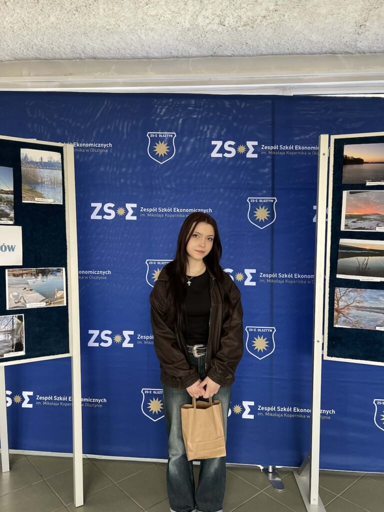 Uczennica przed ścianką promującą szkołę.